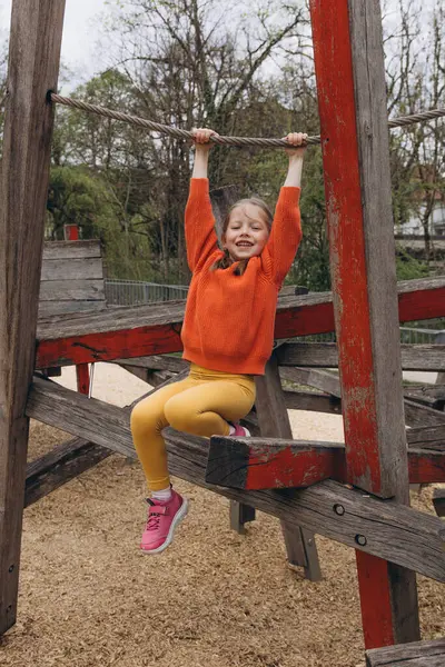 Tahta kirişlerden yapılmış bir oyun parkına tırmanan 5 yaşındaki bir kız yazın açık havada oyun ve maceranın tadını çıkarıyor. Yüksek kalite fotoğraf