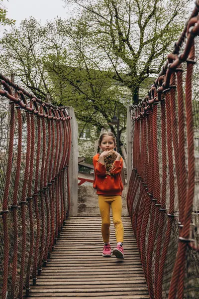 Asılı bir halat köprüsünde koşan genç bir kız, neşeli bir açık hava ortamında enerji ve macera dolu. Yüksek kalite fotoğraf