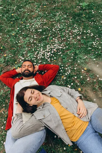 İki insan, kadın ve erkek yazın çimenlikte küçük kır çiçekleriyle birlikte dinleniyor, dışarıda huzurlu bir anın tadını çıkarıyorlar. Günlük giysiler ve doğal çevre sakin ve otantik bir ortam yaratıyor. Yüksek kalite fotoğraf