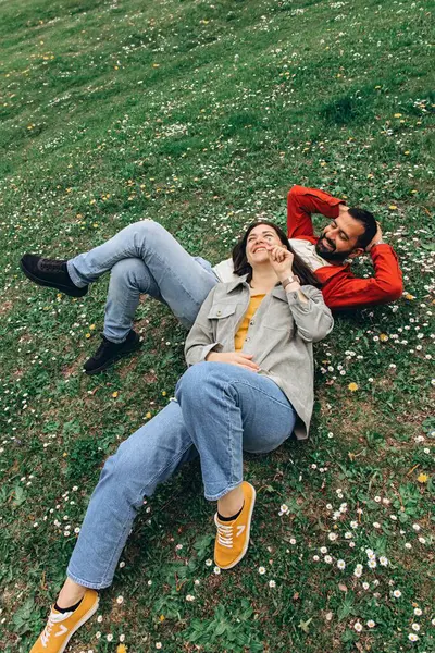 İki insan, kadın ve erkek yazın çimenlikte küçük kır çiçekleriyle birlikte dinleniyor, dışarıda huzurlu bir anın tadını çıkarıyorlar. Günlük giysiler ve doğal çevre sakin ve otantik bir ortam yaratıyor. Yüksek kalite fotoğraf