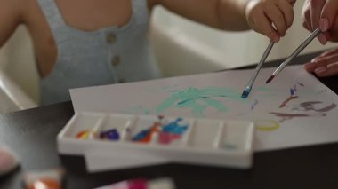 Küçük çocuk yüksek sandalyede oturuyor, kağıt üzerinde parlak renklerle resim yapıyor. Yaratıcı bir çocukluk anı. Yüksek kalite 4k görüntü