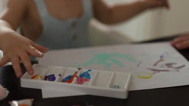 Küçük çocuk yüksek sandalyede oturuyor, kağıt üzerinde parlak renklerle resim yapıyor. Yaratıcı bir çocukluk anı. Yüksek kalite 4k görüntü