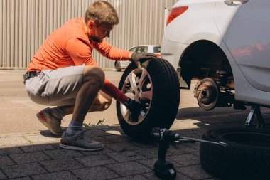 Adam araç gereçleri kullanarak yol kenarında lastik değiştiriyor, araç krikoda kaldırılıyor. Araba tamiri, bakım, arıza yardımı ve gerçek hayat durumları kavramı. Yüksek kalite fotoğraf