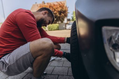 Adam araç gereçleri kullanarak yol kenarında lastik değiştiriyor, araç krikoda kaldırılıyor. Araba tamiri, bakım, arıza yardımı ve gerçek hayat durumları kavramı. Yüksek kalite fotoğraf