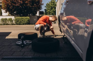Adam araç gereçleri kullanarak yol kenarında lastik değiştiriyor, araç krikoda kaldırılıyor. Araba tamiri, bakım, arıza yardımı ve gerçek hayat durumları kavramı. Yüksek kalite fotoğraf