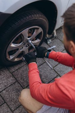 Adam araç gereçleri kullanarak yol kenarında lastik değiştiriyor, araç krikoda kaldırılıyor. Araba tamiri, bakım, arıza yardımı ve gerçek hayat durumları kavramı. Yüksek kalite fotoğraf