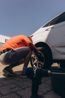 Adam araç gereçleri kullanarak yol kenarında lastik değiştiriyor, araç krikoda kaldırılıyor. Araba tamiri, bakım, arıza yardımı ve gerçek hayat durumları kavramı. Yüksek kalite fotoğraf