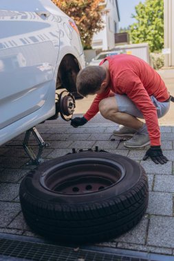 Adam araç gereçleri kullanarak yol kenarında lastik değiştiriyor, araç krikoda kaldırılıyor. Araba tamiri, bakım, arıza yardımı ve gerçek hayat durumları kavramı. Yüksek kalite fotoğraf