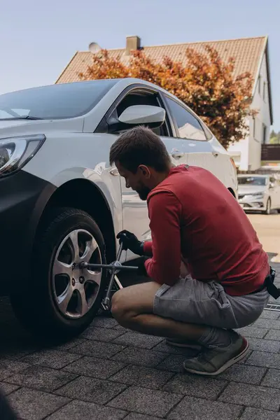 Adam araç gereçleri kullanarak yol kenarında lastik değiştiriyor, araç krikoda kaldırılıyor. Araba tamiri, bakım, arıza yardımı ve gerçek hayat durumları kavramı. Yüksek kalite fotoğraf