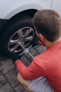 Adam araç gereçleri kullanarak yol kenarında lastik değiştiriyor, araç krikoda kaldırılıyor. Araba tamiri, bakım, arıza yardımı ve gerçek hayat durumları kavramı. Yüksek kalite fotoğraf