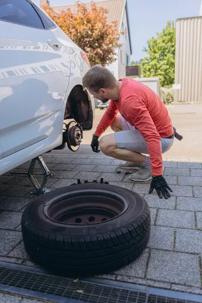 Adam araç gereçleri kullanarak yol kenarında lastik değiştiriyor, araç krikoda kaldırılıyor. Araba tamiri, bakım, arıza yardımı ve gerçek hayat durumları kavramı. Yüksek kalite fotoğraf