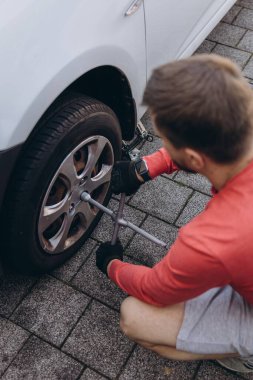 Adam araç gereçleri kullanarak yol kenarında lastik değiştiriyor, araç krikoda kaldırılıyor. Araba tamiri, bakım, arıza yardımı ve gerçek hayat durumları kavramı. Yüksek kalite fotoğraf