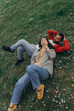 İki insan, kadın ve erkek yazın çimenlikte küçük kır çiçekleriyle birlikte dinleniyor, dışarıda huzurlu bir anın tadını çıkarıyorlar. Günlük giysiler ve doğal çevre sakin ve otantik bir ortam yaratıyor. Yüksek kalite fotoğraf