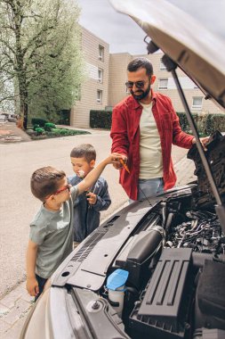 Baba ve oğulları kaputu açık bir şekilde araba tamir ediyorlar. İçten bir bağ kurma, babalık, ebeveynlik, takım çalışması ve öğrenme anı. Babalar Günü 'nü ortak tecrübelerimizle kutluyoruz. Yüksek kalite fotoğraf