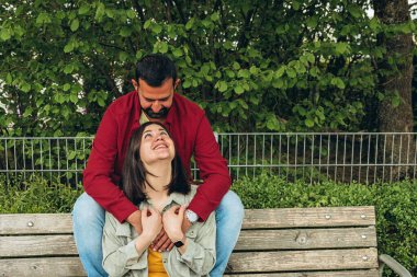 Mutlu çift dışarıda bir bankta oturuyor, gülümsüyor ve birbirlerine sarılıyorlar. Neşeli, sevecen bir an. Sevgiyi, bağlantıyı ve tasasız birlikteliği doğal ortamında yakalıyor. Yüksek kalite fotoğraf