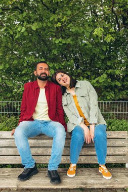 Mutlu çift dışarıda bir bankta oturuyor, gülümsüyor ve birbirlerine sarılıyorlar. Neşeli, sevecen bir an. Sevgiyi, bağlantıyı ve tasasız birlikteliği doğal ortamında yakalıyor. Yüksek kalite fotoğraf