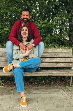 Mutlu çift dışarıda bir bankta oturuyor, gülümsüyor ve birbirlerine sarılıyorlar. Neşeli, sevecen bir an. Sevgiyi, bağlantıyı ve tasasız birlikteliği doğal ortamında yakalıyor. Yüksek kalite fotoğraf