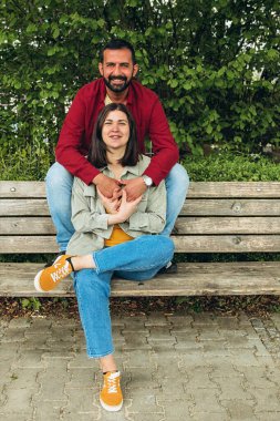 Mutlu çift dışarıda bir bankta oturuyor, gülümsüyor ve birbirlerine sarılıyorlar. Neşeli, sevecen bir an. Sevgiyi, bağlantıyı ve tasasız birlikteliği doğal ortamında yakalıyor. Yüksek kalite fotoğraf