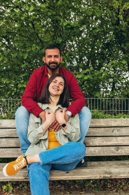 Mutlu çift dışarıda bir bankta oturuyor, gülümsüyor ve birbirlerine sarılıyorlar. Neşeli, sevecen bir an. Sevgiyi, bağlantıyı ve tasasız birlikteliği doğal ortamında yakalıyor. Yüksek kalite fotoğraf