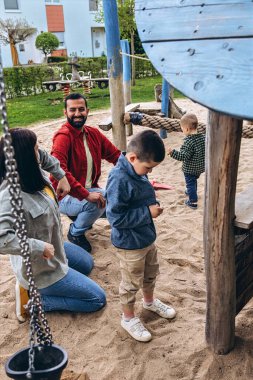 İki oğlu olan ebeveynler oyun alanında kum havuzunda oynuyorlar. Ebeveynlik kavramı, aile bağı, çocukluk etkileşimi ve küçük çocukları birlikte büyütmek ve eğitmek gibi gerçek hayattaki zorluklar. Yüksek kalite fotoğraf