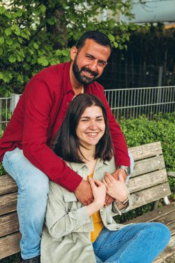 Mutlu çift dışarıda bir bankta oturuyor, gülümsüyor ve birbirlerine sarılıyorlar. Neşeli, sevecen bir an. Sevgiyi, bağlantıyı ve tasasız birlikteliği doğal ortamında yakalıyor. Yüksek kalite fotoğraf