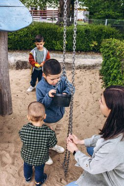 Üç oğlu olan bekar bir anne oyun parkında oyun oynuyor. Aile teması, annelik, ebeveynlik sorunları ve açık havada güçlü, şefkatli, çoklu çocuklu bir ebeveynin günlük hayatı. Yüksek kalite fotoğraf