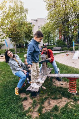 Anne, baba ve iki oğluyla birlikte parkta salıncakta sallanan mutlu bir aile. Açık havada bir bağ kurma, oynama ve çocukluk deneyimini paylaşma anı. Yüksek kalite fotoğraf