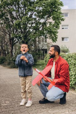 Baba ve oğul parkta yürürken kırmızı oyuncak bir uçak fırlatır ve karahindiba üflerler. Ebeveynlik konsepti, açık hava aile aktiviteleri, bağ kurma, çocukluk anıları, birlikte boş zaman geçirme. Yüksek kalite fotoğraf
