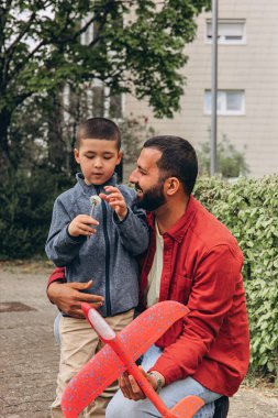 Baba ve oğul parkta yürürken kırmızı oyuncak bir uçak fırlatır ve karahindiba üflerler. Ebeveynlik konsepti, açık hava aile aktiviteleri, bağ kurma, çocukluk anıları, birlikte boş zaman geçirme. Yüksek kalite fotoğraf