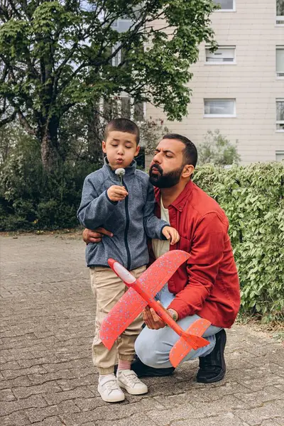 Baba ve oğul parkta yürürken kırmızı oyuncak bir uçak fırlatır ve karahindiba üflerler. Ebeveynlik konsepti, açık hava aile aktiviteleri, bağ kurma, çocukluk anıları, birlikte boş zaman geçirme. Yüksek kalite fotoğraf