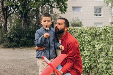 Baba ve oğul parkta yürürken kırmızı oyuncak bir uçak fırlatır ve karahindiba üflerler. Ebeveynlik konsepti, açık hava aile aktiviteleri, bağ kurma, çocukluk anıları, birlikte boş zaman geçirme. Yüksek kalite fotoğraf
