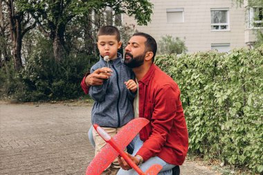 Baba ve oğul parkta yürürken kırmızı oyuncak bir uçak fırlatır ve karahindiba üflerler. Ebeveynlik konsepti, açık hava aile aktiviteleri, bağ kurma, çocukluk anıları, birlikte boş zaman geçirme. Yüksek kalite fotoğraf