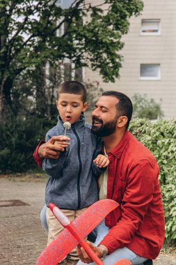 Baba ve oğul parkta yürürken kırmızı oyuncak bir uçak fırlatır ve karahindiba üflerler. Ebeveynlik konsepti, açık hava aile aktiviteleri, bağ kurma, çocukluk anıları, birlikte boş zaman geçirme. Yüksek kalite fotoğraf