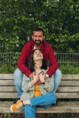Mutlu çift dışarıda bir bankta oturuyor, gülümsüyor ve birbirlerine sarılıyorlar. Neşeli, sevecen bir an. Sevgiyi, bağlantıyı ve tasasız birlikteliği doğal ortamında yakalıyor. Yüksek kalite fotoğraf