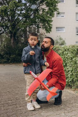 Baba ve oğul parkta yürürken kırmızı oyuncak bir uçak fırlatır ve karahindiba üflerler. Ebeveynlik konsepti, açık hava aile aktiviteleri, bağ kurma, çocukluk anıları, birlikte boş zaman geçirme. Yüksek kalite fotoğraf