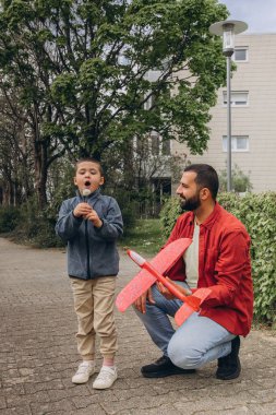 Baba ve oğul parkta yürürken kırmızı oyuncak bir uçak fırlatır ve karahindiba üflerler. Ebeveynlik konsepti, açık hava aile aktiviteleri, bağ kurma, çocukluk anıları, birlikte boş zaman geçirme. Yüksek kalite fotoğraf