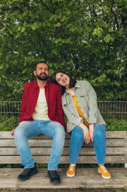 Mutlu çift dışarıda bir bankta oturuyor, gülümsüyor ve birbirlerine sarılıyorlar. Neşeli, sevecen bir an. Sevgiyi, bağlantıyı ve tasasız birlikteliği doğal ortamında yakalıyor. Yüksek kalite fotoğraf