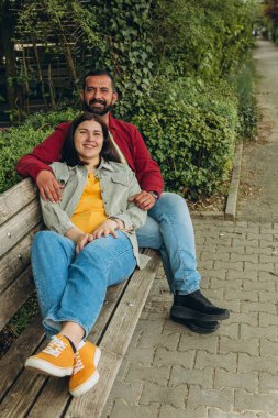 Mutlu çift dışarıda bir bankta oturuyor, gülümsüyor ve birbirlerine sarılıyorlar. Neşeli, sevecen bir an. Sevgiyi, bağlantıyı ve tasasız birlikteliği doğal ortamında yakalıyor. Yüksek kalite fotoğraf