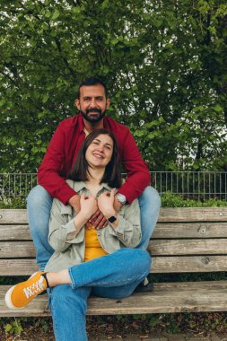 Mutlu çift dışarıda bir bankta oturuyor, gülümsüyor ve birbirlerine sarılıyorlar. Neşeli, sevecen bir an. Sevgiyi, bağlantıyı ve tasasız birlikteliği doğal ortamında yakalıyor. Yüksek kalite fotoğraf