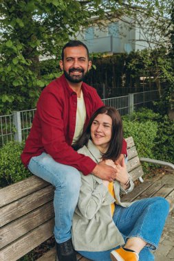 Mutlu çift dışarıda bir bankta oturuyor, gülümsüyor ve birbirlerine sarılıyorlar. Neşeli, sevecen bir an. Sevgiyi, bağlantıyı ve tasasız birlikteliği doğal ortamında yakalıyor. Yüksek kalite fotoğraf