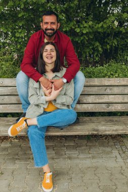 Mutlu çift dışarıda bir bankta oturuyor, gülümsüyor ve birbirlerine sarılıyorlar. Neşeli, sevecen bir an. Sevgiyi, bağlantıyı ve tasasız birlikteliği doğal ortamında yakalıyor. Yüksek kalite fotoğraf