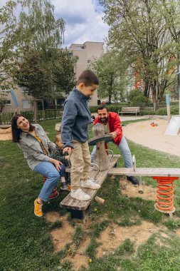 Anne, baba ve iki oğluyla birlikte parkta salıncakta sallanan mutlu bir aile. Açık havada bir bağ kurma, oynama ve çocukluk deneyimini paylaşma anı. Yüksek kalite fotoğraf