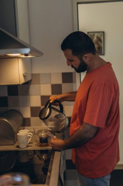 Babam sessiz bir sabahta mutfakta çay yapıyor. Sahne, aile sorumluluğunu, sakin rutini ve aile hayatındaki erkek rollerine modern bir bakış açısını yansıtıyor. Yüksek kalite fotoğraf