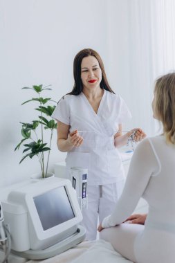 Modern güzellik kliniğinde vücut hatları çizilmeden ya da anti-selülit tedavisinden önce kadın müşteriye bant danışarak gülümseyen kozmetolog. Yüksek kalite fotoğraf