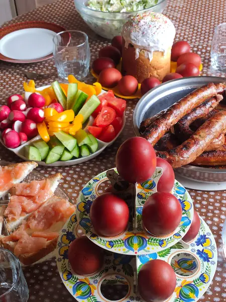Easter lunch with dyed red eggs, sausages, cucumbers, tomatoes, radishes, sandwich on plates on a stand