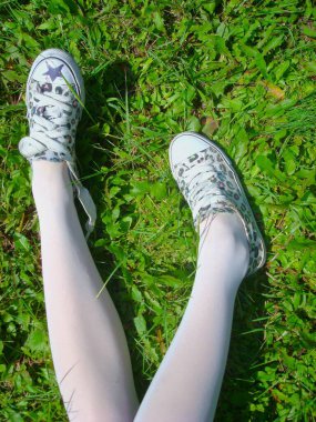 Beyaz spor ayakkabılar ve beyaz taytlarla kızın bacakları çimlerin üzerinde