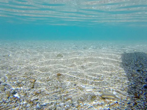 Su altı deniz manzarası, pürüzsüz mavi su ve taş çakıl taşları kum. Deniz kabukları, deniz kıyısı.