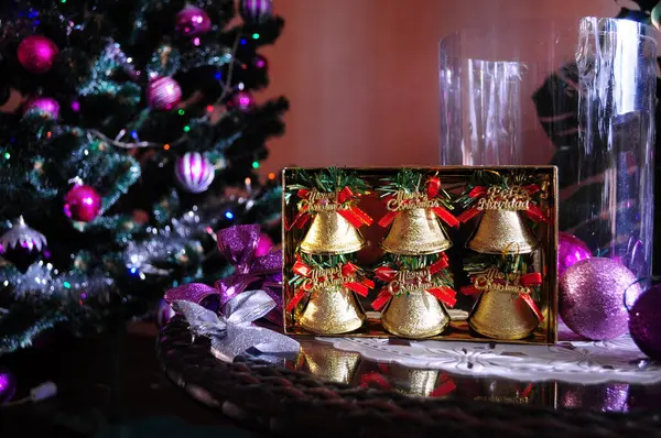 Yeşil dallar ve kırmızı fiyonklarla süslenmiş altın zillerle süslü yeni yıl kompozisyonu. Mor ve gümüş topları, çelenkleri ve renkli ışıkları olan zarif bir Noel ağacı, neşeli bir atmosfer. Dekoratif kurdeleler ve parlak Noel oyuncakları
