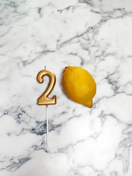 Mermer yüzeyde 2 numara şeklinde altın bir mum ve bir limon bulunur. kompozisyon, 2 milyon, blog yazarı, kutlama, aboneler