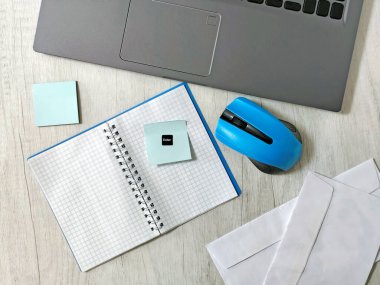 Laptoplu iş yeri, mavi kablosuz fare, zarflar, defter, ofis masası, ahşap masadaki yapışkan notlar. İş, planlama, uzaktan çalışma konsepti, serbest çalışma, eğitim